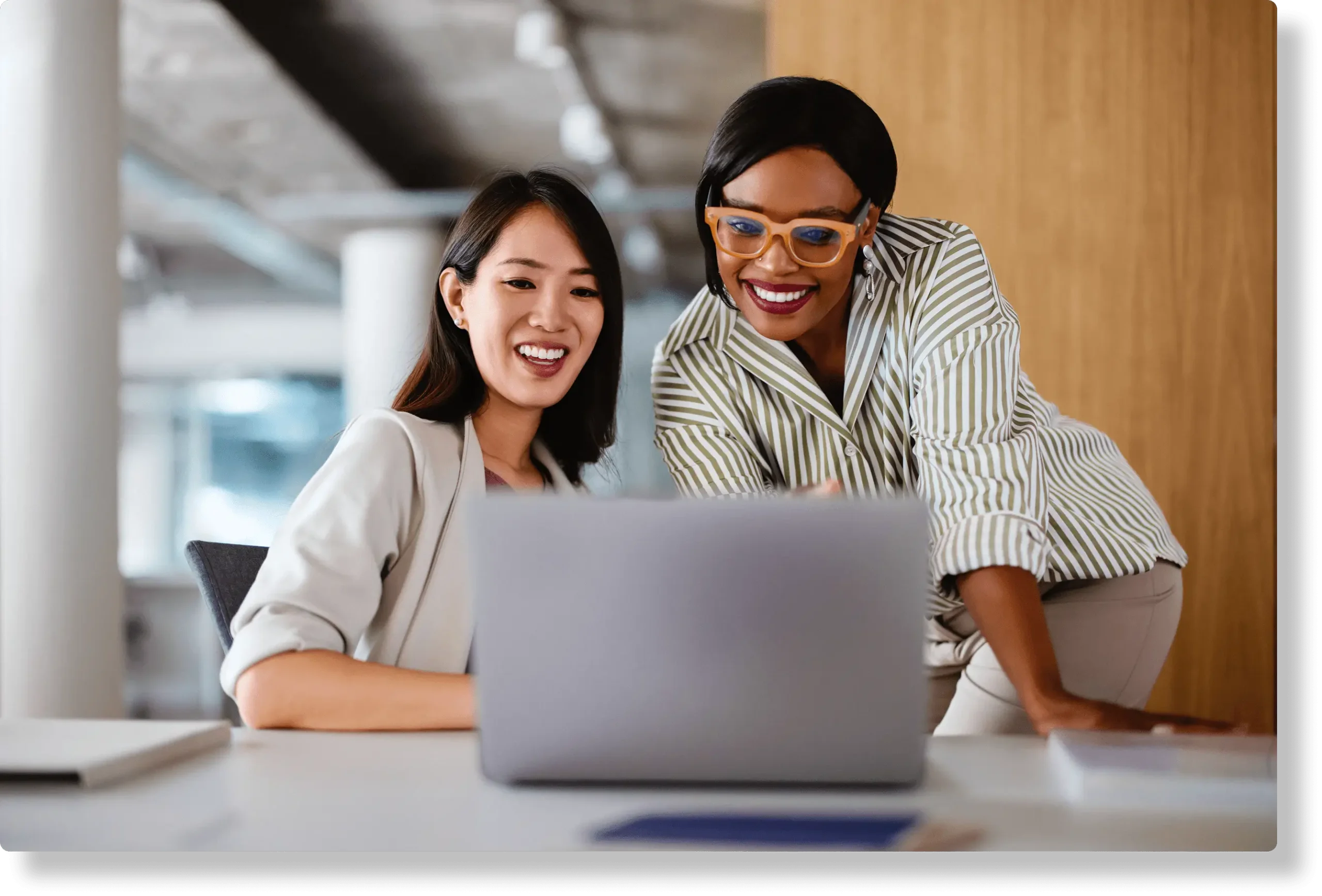Two females colleagues in front of a laptop smiling as they work together on a project