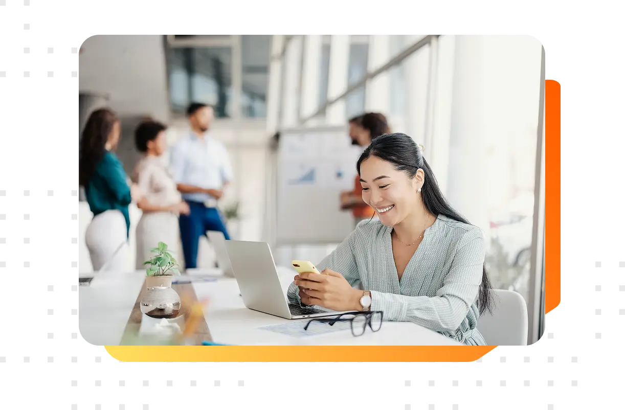 A female in the foreground viewing her smartphone with her colleagues in the background of the office space