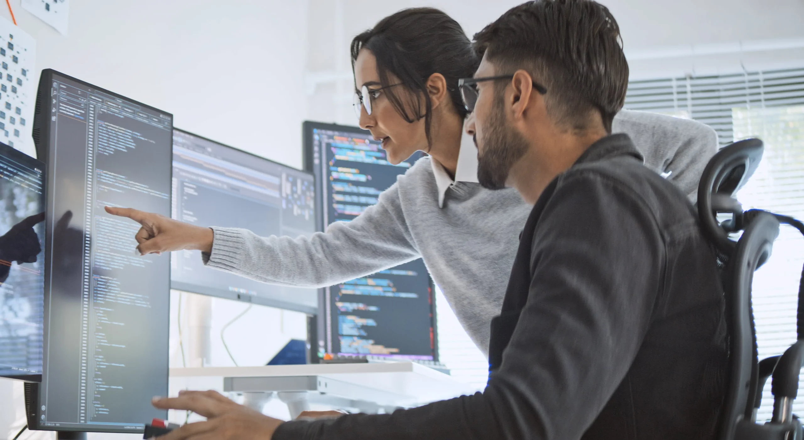 male and female developers working together in an office space on a large computer monitor
